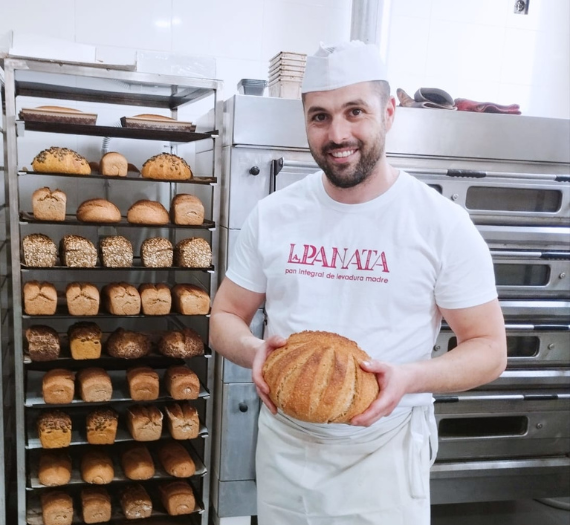 foto dueño panadería mostrando un pan y con fondo panes